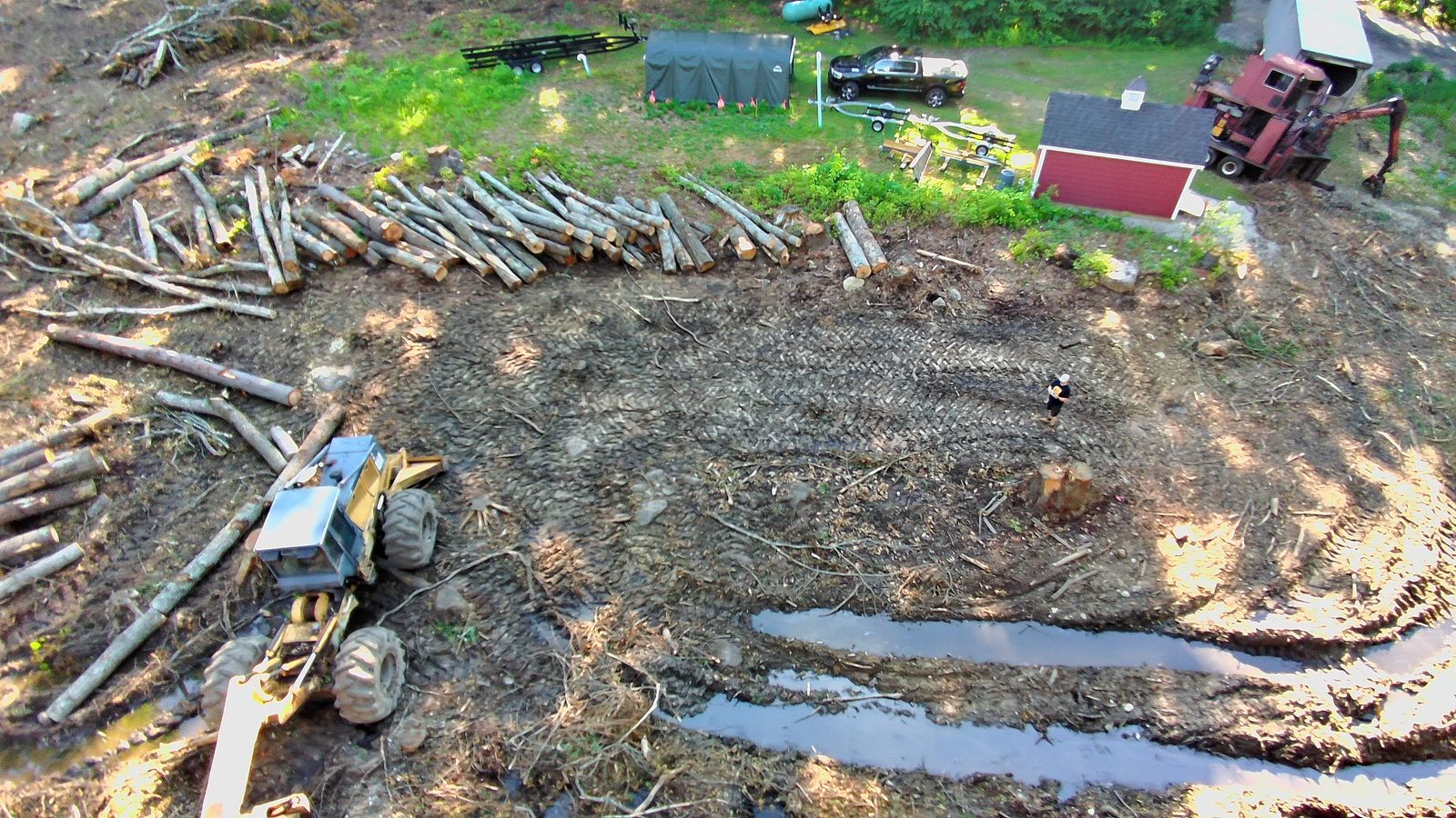 Aerial of the logging operation looking north — skidder, stacked logs, and equipment